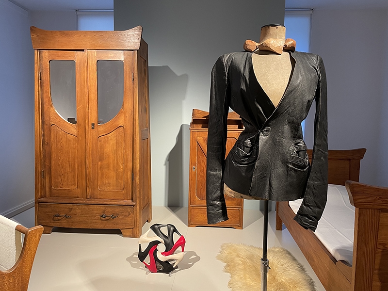 Exhibition view, Jewellery & Garment. (On mannequin) jewelry: Dorothea Prühl, Birds in Winter, 2016, necklace, cherry wood. Garment: Rick Owens, leather jacket, 2000s, displayed in the Bröhan Museum’s bedroom of a North Sea sanatorium, as an example of German Reform Art around 1900. (On floor) Lisa Walker: Fischli and Weiss bracelet, 2018, shoes