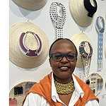 Artist Jennifer Mulli, who is from Kenya, wears her vertebrae necklace, made of brass, while standing in front of beaded necklaces and hats made by women in the village of Ukambani. The vertebrae is essential to a person, “and that’s what a woman is—the spine that holds a nation together,” says Mulli. Photo: Jennifer Altmann