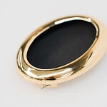 Jasmijn Van Hoof, <em>Abyss,</em> 2024, brooch in gold-plated brass, pigment, steel wire, photo courtesy of the artist | This brooch refers to total forgetting: the black hole or the abyss. “The oval is taken from photo frames that I reworked,” states Van Hoof. “Looking at the brooch from the front, total forgetting is actually framed as a portrait on the cabinet. Whereas we show important elements with portrait photos, this brooch shows that total forgetting is important. It is partly so that our brains have room to make new memories.”