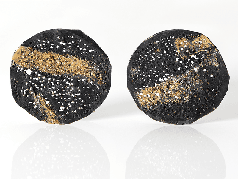 Gigi Mariani, Corrosion series, 2025, earrings in silver, 18-karat yellow gold, niello, patina, 1 inch (26 mm) in diameter, photo courtesy of Thereza Pedrosa Gallery