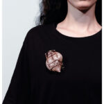 Caption: Svea Finck, ReFLectME, 2025, brooch in glass, copper, model: Rune Vervoort, photo: Saverio Sammartino