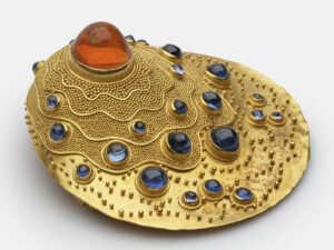 Elisabeth Treskow (designer), Gertrud Weber-Vogel (fabricator), Untitled, 1967, brooch in gold (embossing, granulation), sapphire, fire opal, ¾ x 1 ¾ x 1 ¾ inches (19.8 x 44.6 x 44 mm), on permanent loan from the Overstolzengesellschaft, photo: MAKK / DetlefSchumacher.com