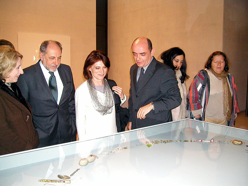 Cristina Filipe et al., A Chain for Tereza, necklace in various materials, 63 inches (160 cm) in diameter, photo courtesy of Ar.Co – Centro de Arte e Comunicação Visual. The photo was taken at the opening of the exhibition Meeting Point(s) 1978–2003. 25 Years of Interventions in the Jewelry Department of Ar.Co, held at CAM – Centro de Arte Moderna (Modern Art Center), Calouste Gulbenkian Foundation, Lisbon, 2004, when Tereza Seabra was given the piece. (Left to right) Emílio Rui Vilar, president of the Calouste Gulbenkian Foundation; Tereza Seabra; Manuel Castro Caldas, the director of Ar.Co.