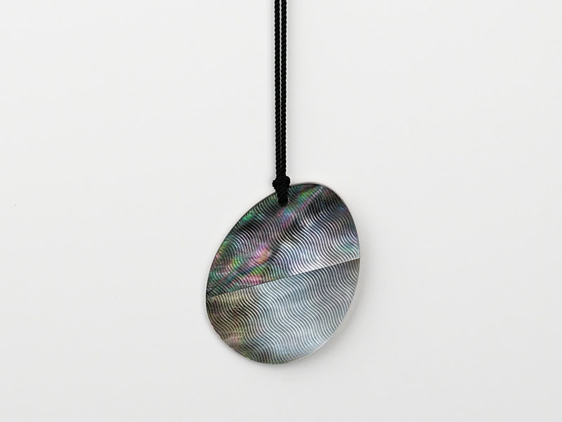 Zhipeng Wang, Guilloché Egg #17, 2025, pendant in mother-of-pearl, sterling silver, string, 2 ⅛ x 1 ⅝ x ⅛ inches (55 x 41 x 3 mm), photo courtesy of the artist